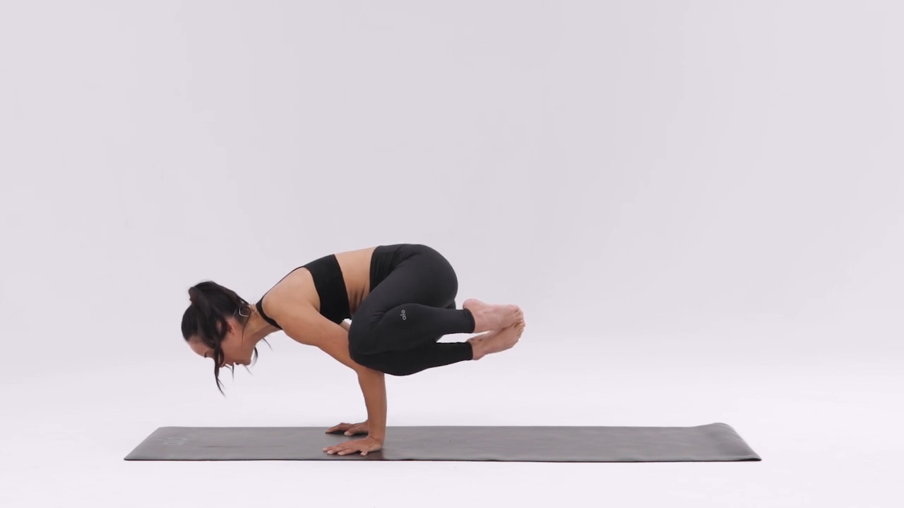 person performing Side Crow Pose (Parsva Bakasana) on a yoga mat, balancing on one arm with legs twisted to the side